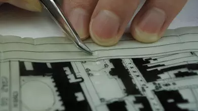 Close-up photograph of a small splint repair of Japanese kozo tissue being applied with tweezers to an architectural plan on plastic film.